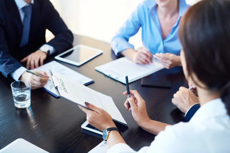 Unrecognizable business partners discussing agreement conditions reviewing it together at meeting